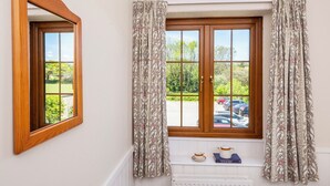 A room with a large window, a mirror, and a shelf with a book and a teapot. - The Hayloft (Falmouth)