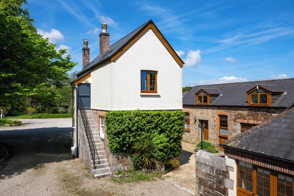 Un bâtiment blanc, doté d’une petite fenêtre et d’une cheminée, est situé à côté d’un bâtiment en pierre dont le toit est sombre.