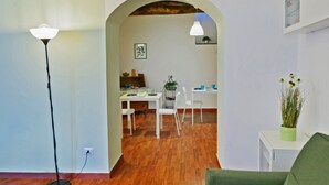 Un salon moderne avec un canapé vert, un coin repas avec des chaises blanches et une cuisine visible à travers une arche.