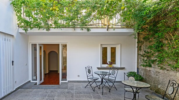Une cour avec une table et des chaises, une fenêtre et une porte donnant sur un espace intérieur.