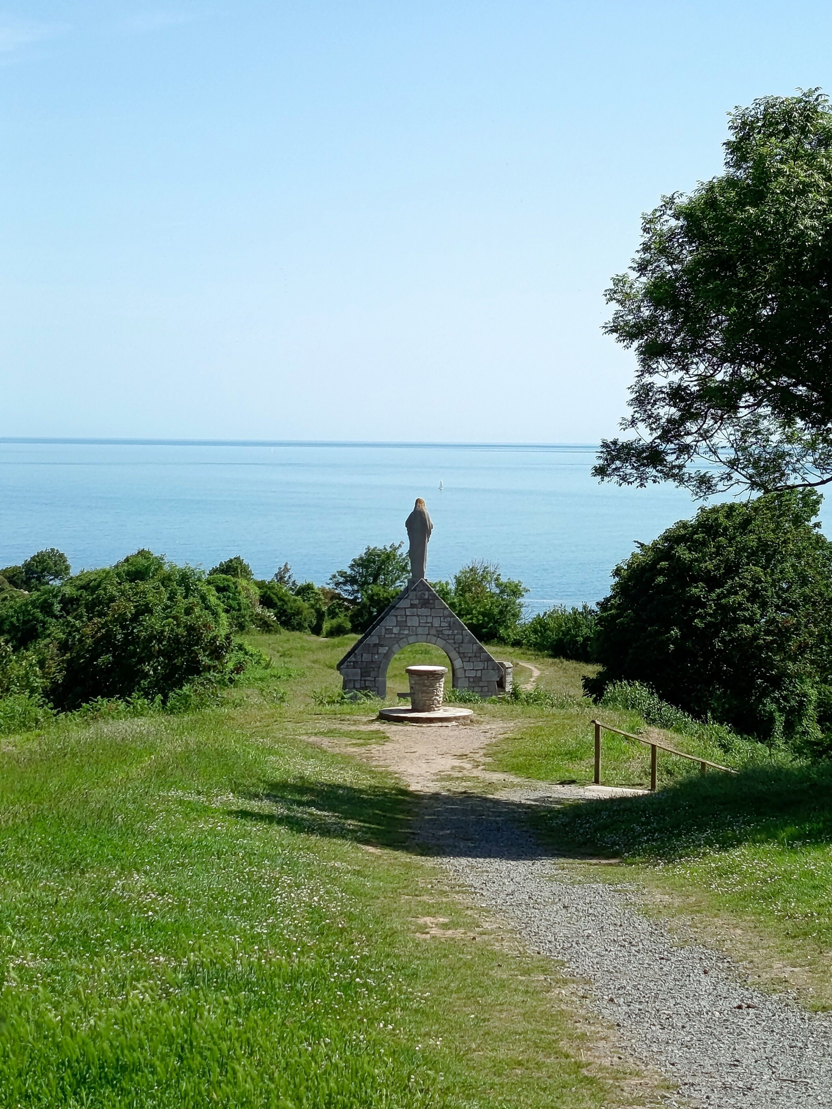 A stone monument with a circular base, surrounded by a grassy area with a clear view of the sea.