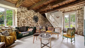 A rustic interior with stone walls, a wooden ceiling, a round table, and a staircase. - Spacious Family Home with Private Terrace, Garden & Wi-Fi in Saint Lormel (Saint Lormel)