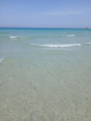 Ein sauberer Strand mit ruhigem Wasser und fernen Felsenformationen.
