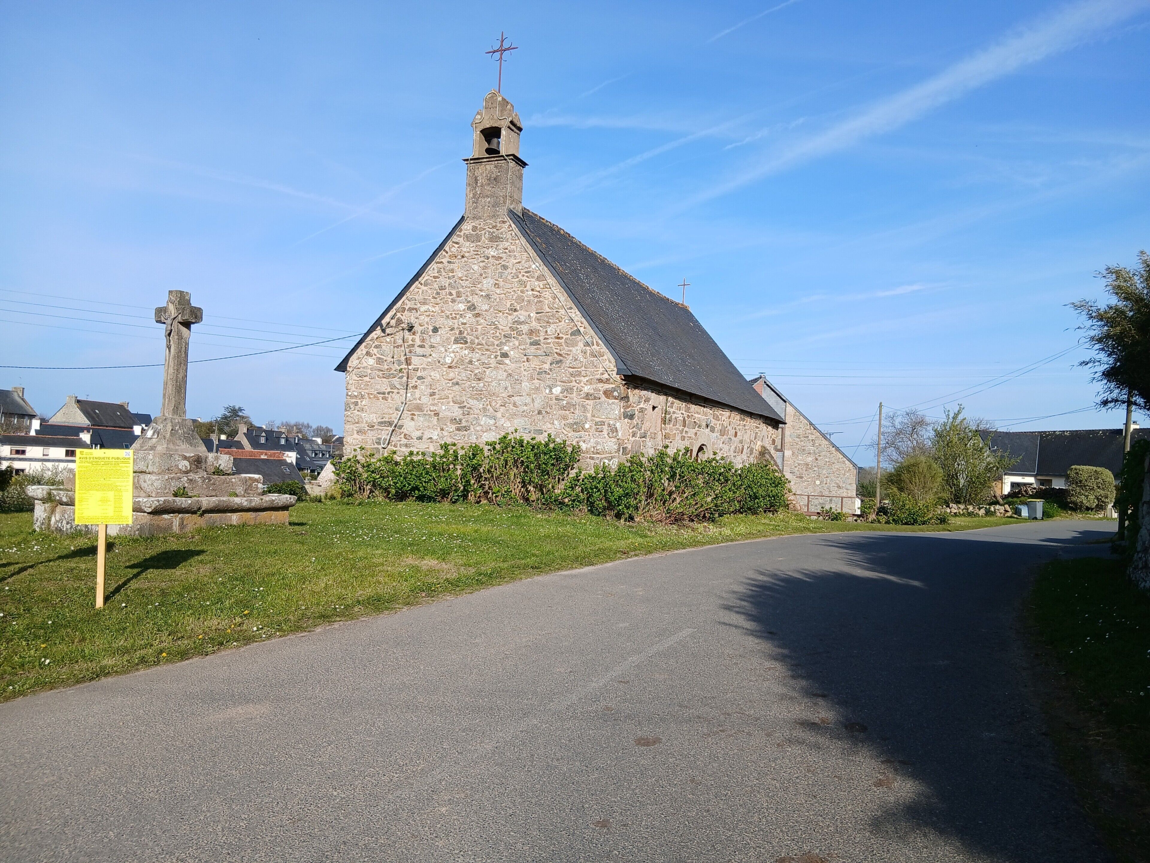 A stone church with a cross on top, a grassy area in front, and a road leading away.