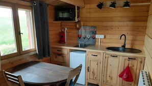 A wooden cabin with a kitchen, dining table, chairs, and a window with curtains.