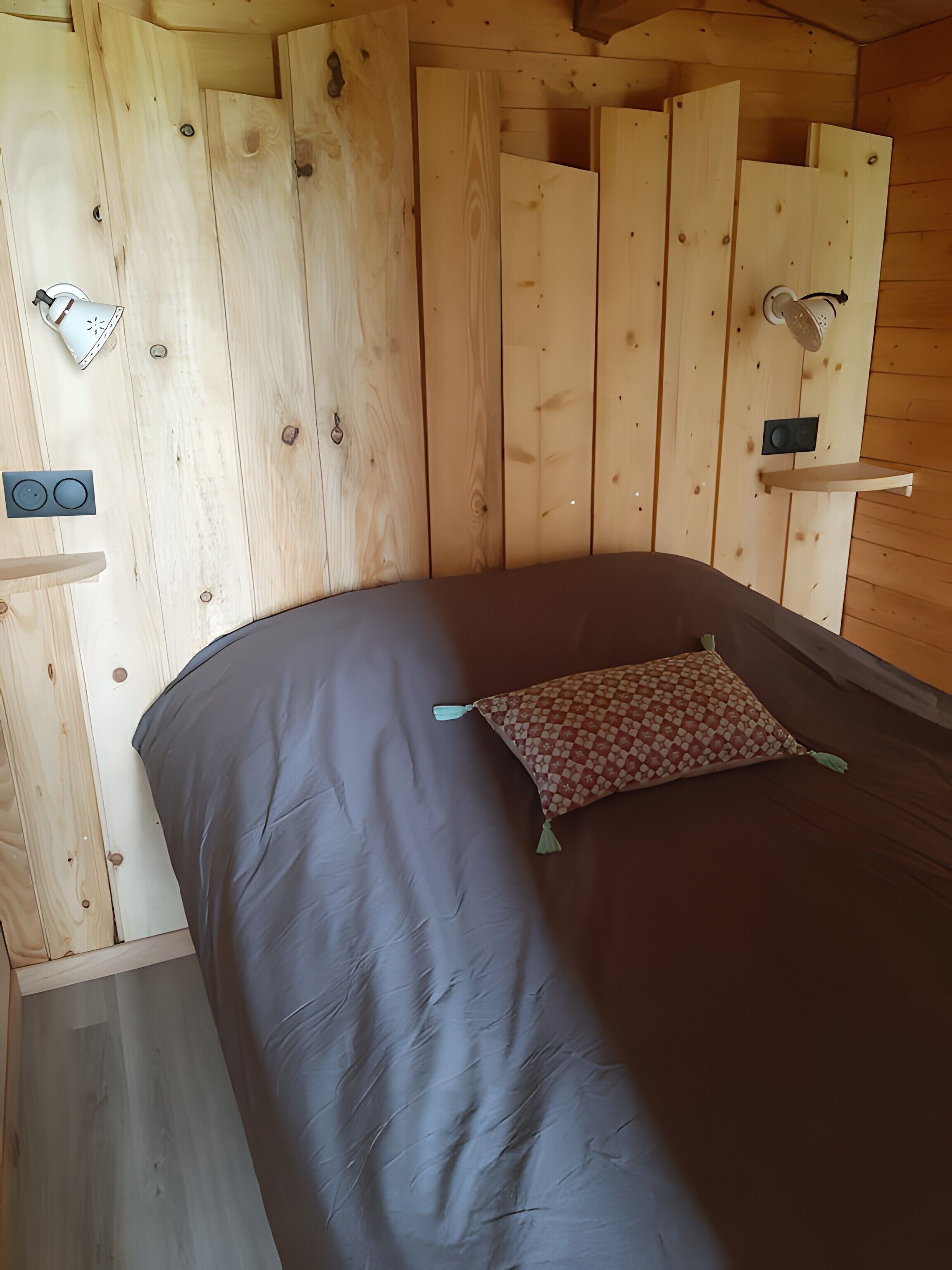 A wooden cabin interior with a bed, a small shelf, and a wall-mounted speaker.
