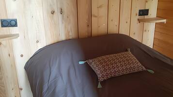 A wooden cabin interior with a bed, a small shelf, and a wall-mounted speaker.