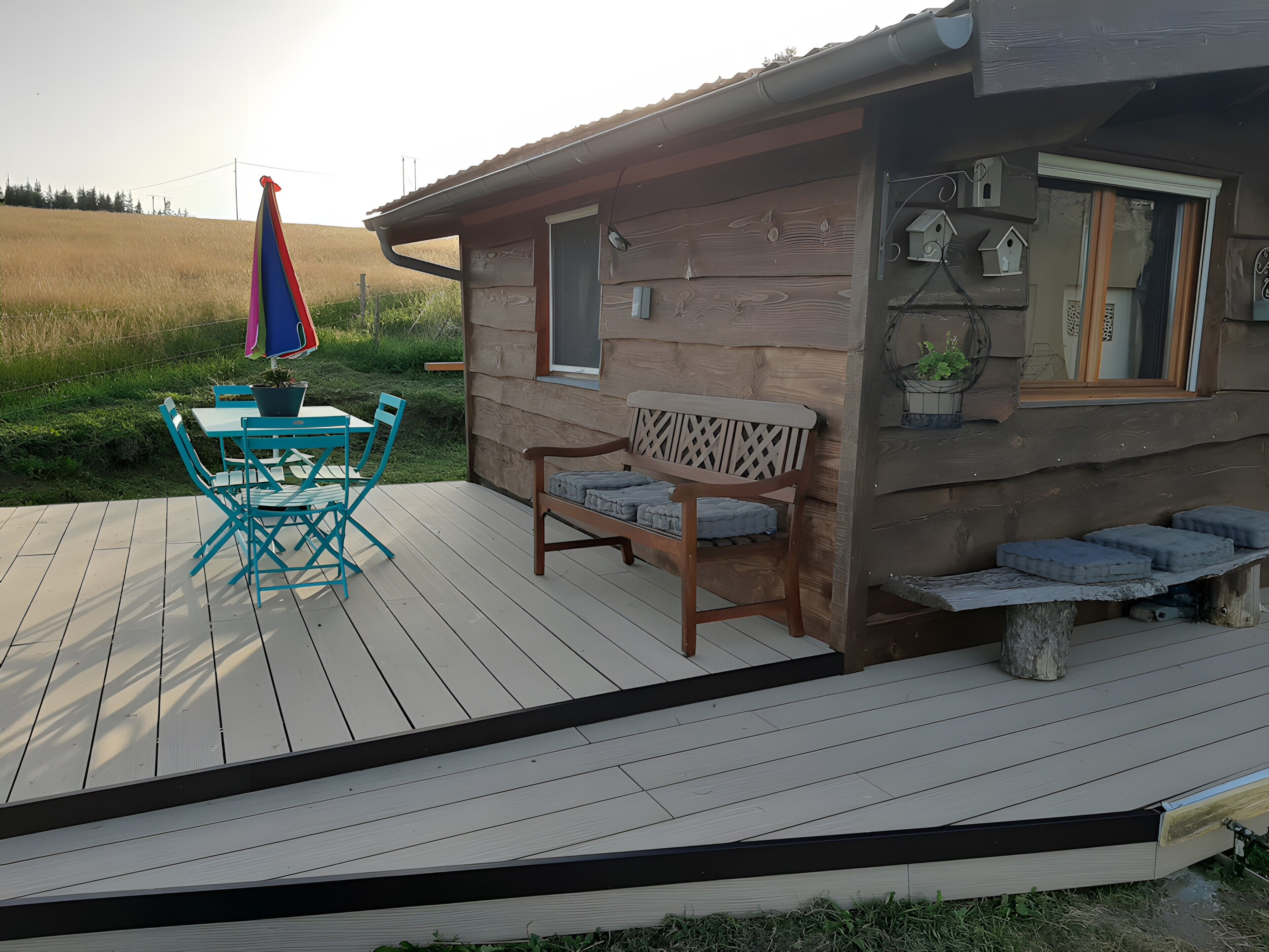 Een houten chalet met een terras, een tafel met stoelen en een bank.