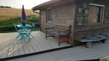 Een houten chalet met een terras, een tafel met stoelen en een bank.