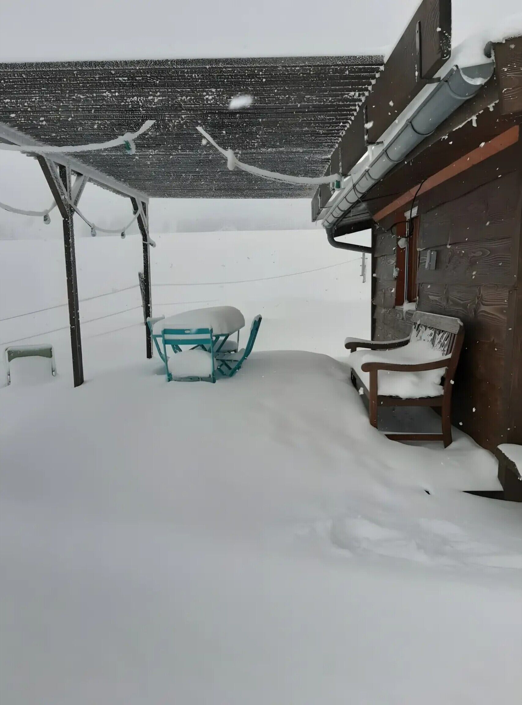 Un espacio exterior cubierto de nieve con un banco de madera y una silla de metal.