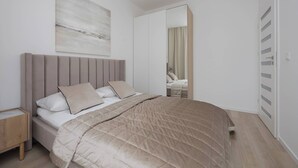 A modern bedroom with a bed, a nightstand, a large mirror, and a painting on the wall. - Stylish Apartment with Balcony | Air Conditioning | Close to the Metro (Warszawa)