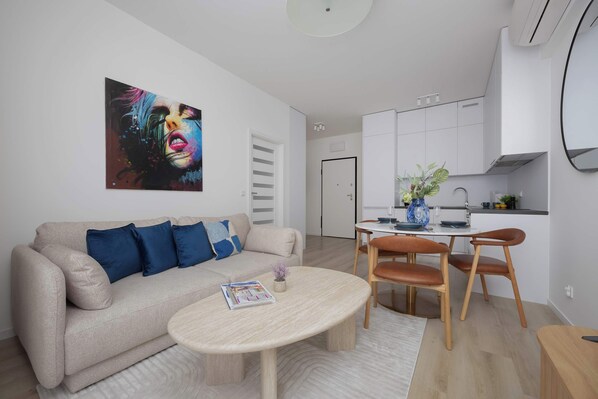 Een moderne woonkamer met een beige bank, blauwe kussens, een bijzettafeltje en een levendig abstract schilderij.