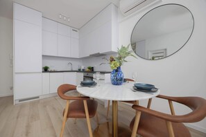 Een moderne keuken met witte kasten, een ronde eettafel met bruine stoelen en een blauwe vaas met bloemen.