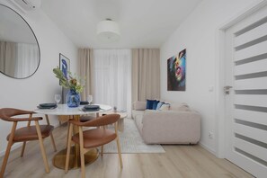 Ein modernes Wohnzimmer mit einem runden Esstisch, braunen Ledersesseln, einem beige farbenen Sofa und einem farbenfrohen abstrakten Gemälde an der Wand.