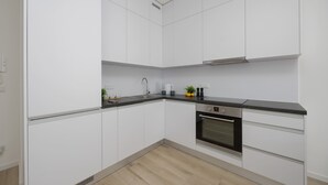 A modern kitchen with white cabinets, a black countertop, and a built-in oven. - Stylish Apartment with Balcony | Air Conditioning | Close to the Metro (Warszawa)