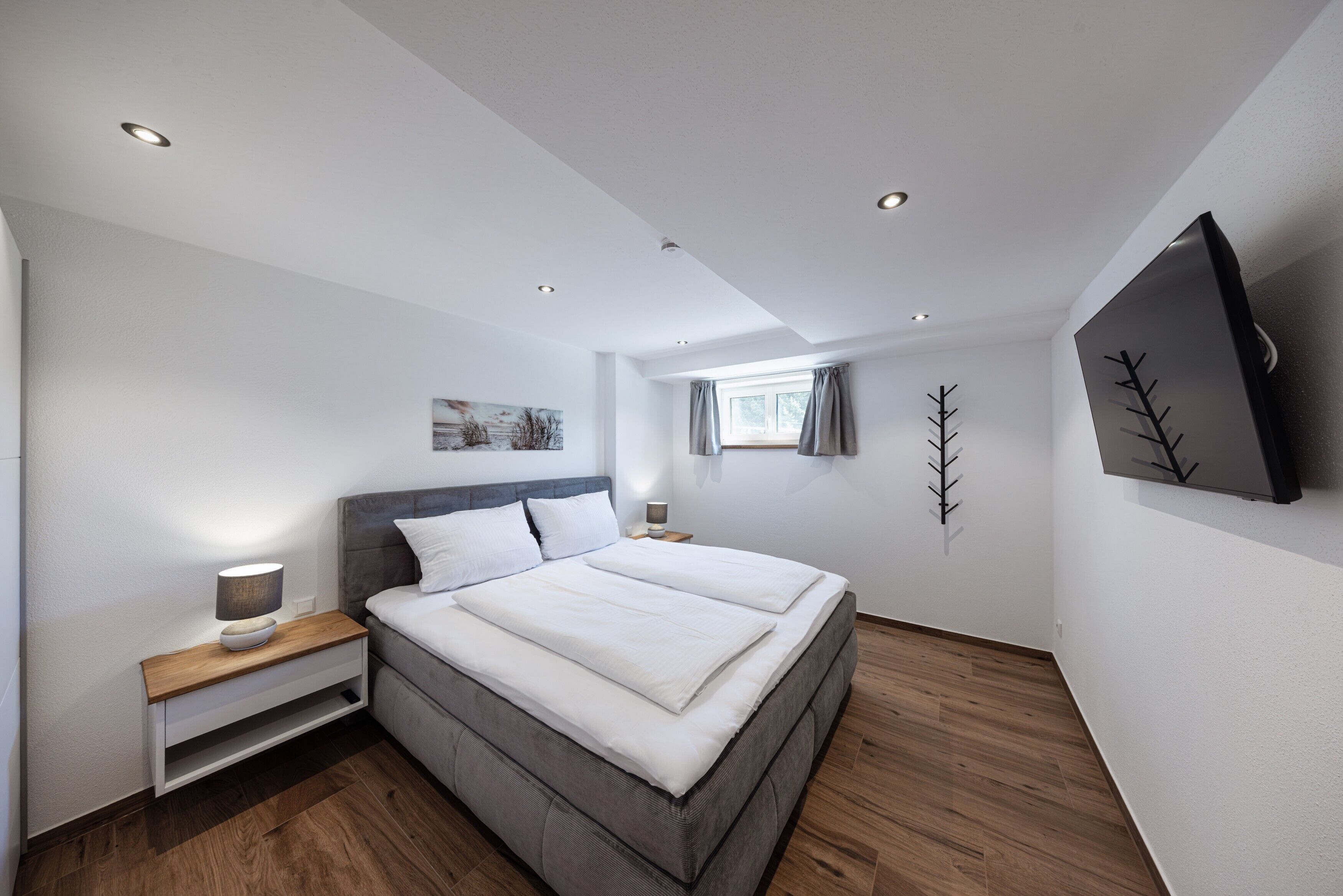 A modern bedroom with a large bed, bedside tables, a flat-screen TV, and a window with curtains.