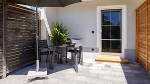 An outdoor patio with a table and chairs, a potted plant, and a wooden bench. - Holiday Apartment for 2 with Private Terrace, Shared Garden & Wi-Fi at Ferienhaus Waldherr (Waging am See)