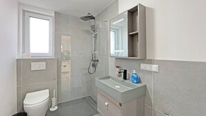 A modern bathroom with a toilet, sink, shower, and a mirror above the vanity. - Apartment '5' with Private Terrace, Shared Garden and Wi-Fi (Ichenhausen)