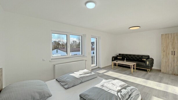 A modern bedroom with a bed, a sofa, a wooden wardrobe, and a window with a view. - Apartment '5' with Private Terrace, Shared Garden and Wi-Fi (Ichenhausen)
