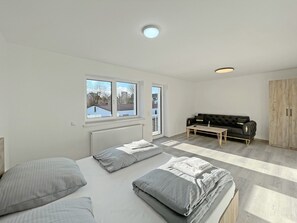 Un dormitorio moderno con cama, sofá, armario de madera y ventana con vistas.