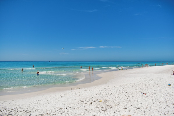 A wide sandy beach with clear blue water and a few people in the distance.