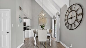 A dining area with a chandelier, a large wall clock, and a view into the kitchen. - Beach Condo~Free Golf Cart~3BD~2BA~Sleeps 8~Balcony~Walk to Beach~Pool (Miramar Beach)