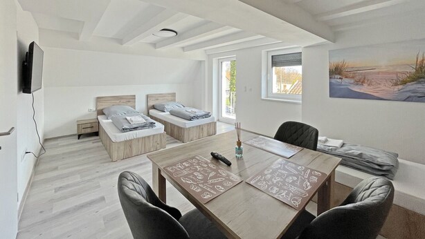 A modern bedroom with two beds, a dining table, and a painting on the wall. - Apartment '6' with Private Terrace, Shared Garden and Wi-Fi (Ichenhausen)