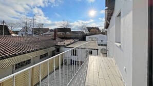 A residential building with a tiled roof, a balcony with a metal railing, and a clear sky with the sun visible. - Apartment '6' with Private Terrace, Shared Garden and Wi-Fi (Ichenhausen)