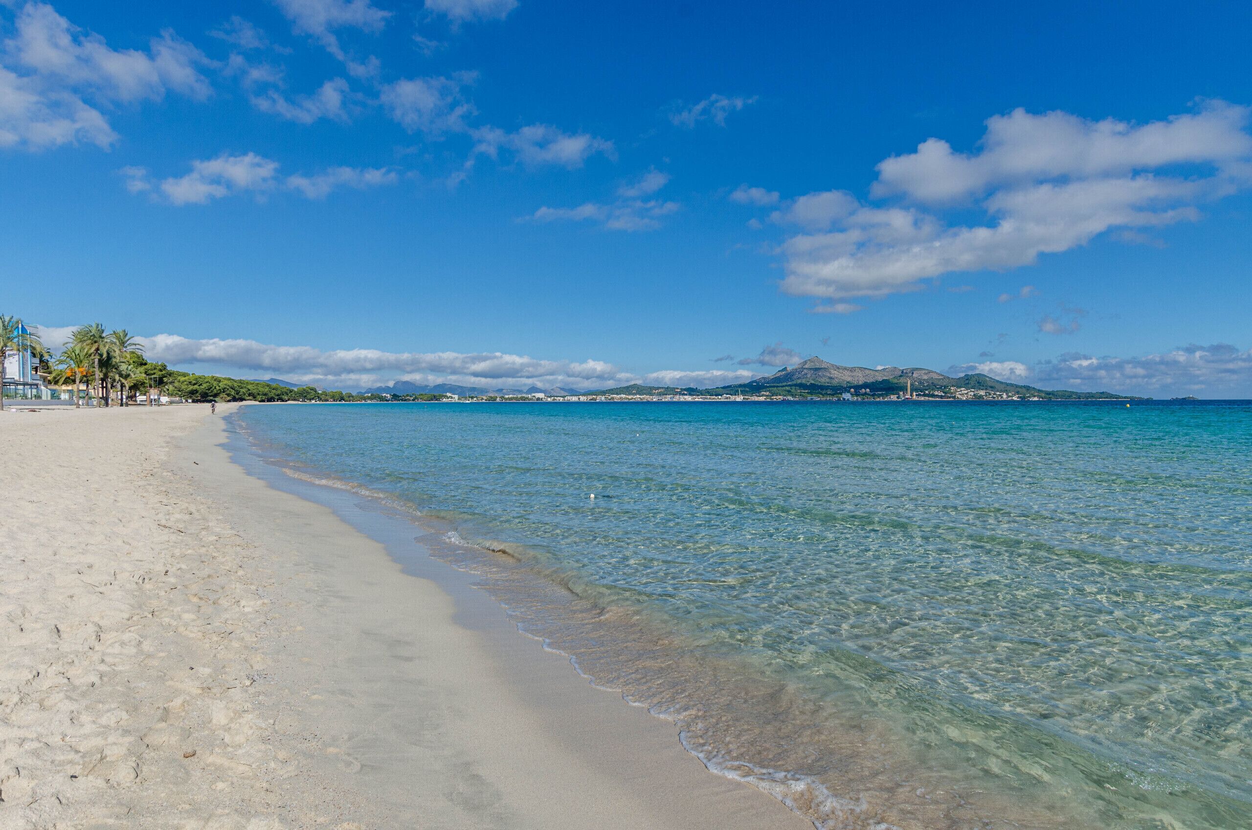 A beach with clear water, a sandy shore, and a distant mountain.