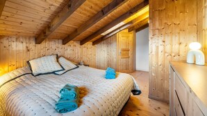 A wooden cabin bedroom with a bed, pillows, and a folded towel. - Le Petiot - mini chalet - maxi douceur - 4p (Haute-Nendaz)