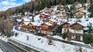 A cluster of wooden cabins with balconies, set on a snowy hillside with a road in the foreground. - Le Petiot - mini chalet - maxi douceur - 4p (Haute-Nendaz)