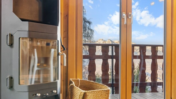 A kitchen with a stove, a wicker basket, and a sliding glass door leading to a balcony with a wooden fence and a mountain view. - Le Petiot - mini chalet - maxi douceur - 4p (Haute-Nendaz)