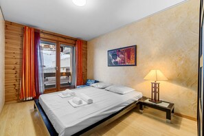 Un dormitorio con cama, una mesita de noche con lámpara, un cuadro en la pared y una ventana con cortinas.