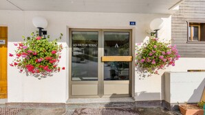Entrada de un edificio con puerta de cristal, un letrero que dice "LES HAUTS DE NENDAZ" y el número "44" sobre la puerta.