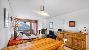 Un área de comedor con una mesa y sillas de madera, una chimenea, un televisor y vistas de montañas a través de una ventana.