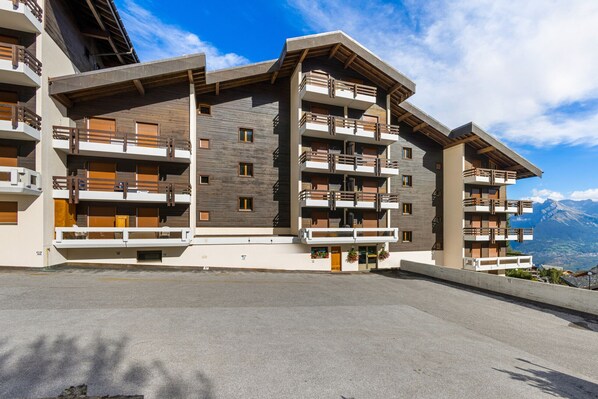 Un hotel de varios pisos con balcones, vistas a montañas y cielo despejado.