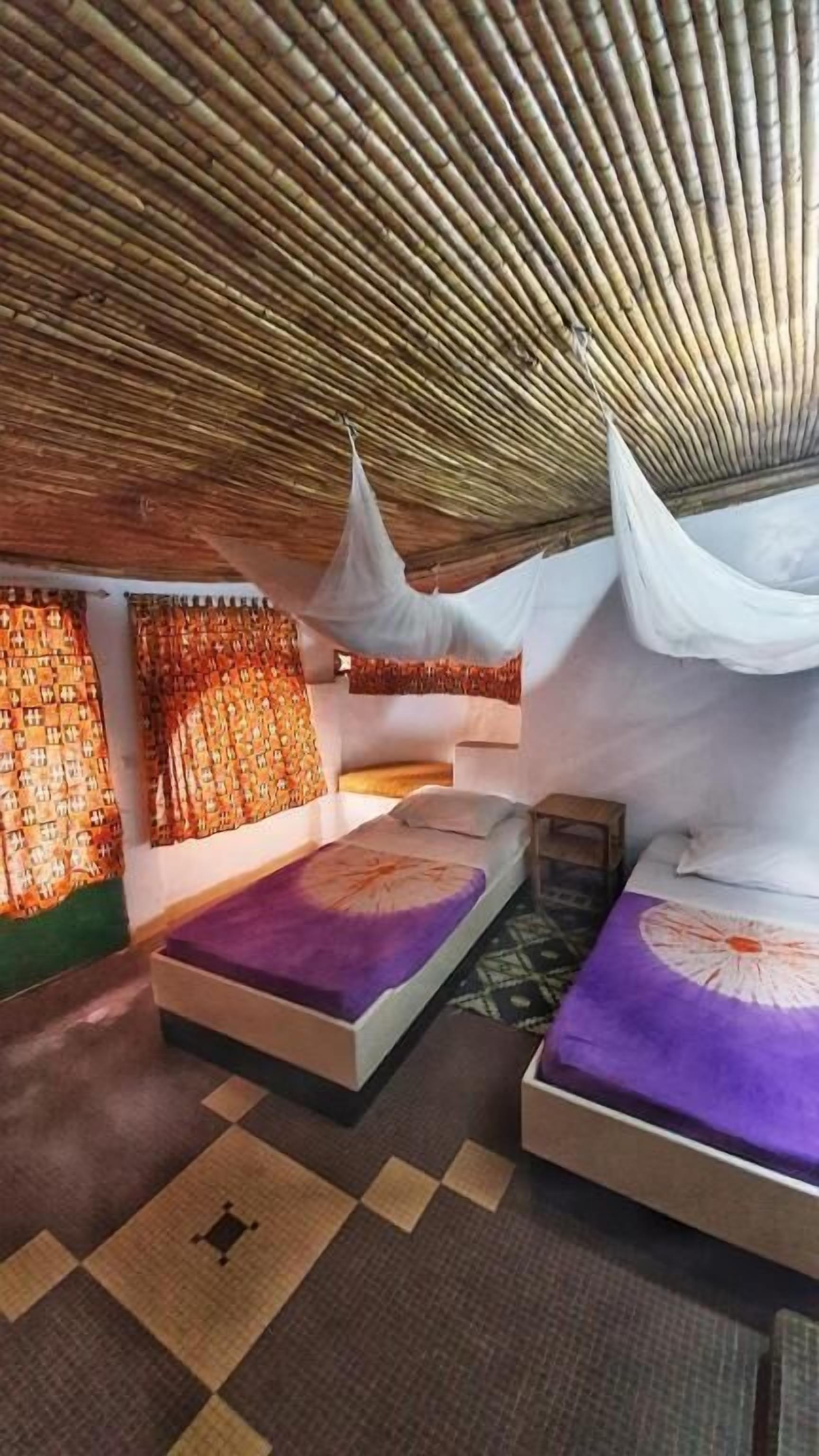 Een kamer met een schuine balkenlaag, een bed met een paars sprei en een kamerbreed tapijt met dessin.