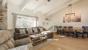 En rummelig stue med stor sofa, sofabord og spiseområde med stole og et træbord.