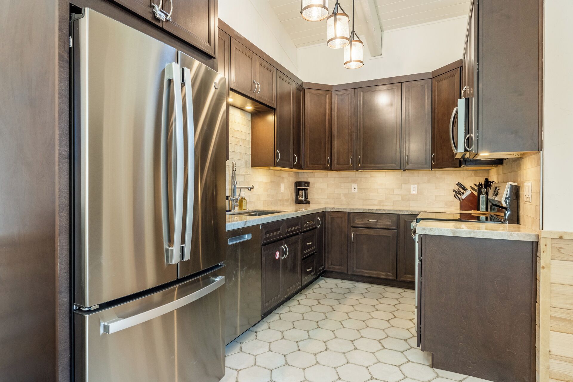 A modern kitchen with dark wooden cabinets, stainless steel appliances, and a hexagonal tile floor.