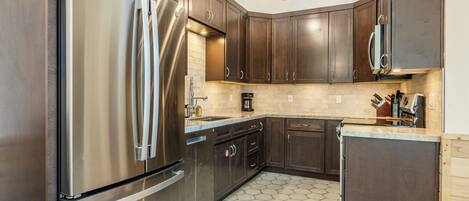 A modern kitchen with dark wooden cabinets, stainless steel appliances, and a hexagonal tile floor.