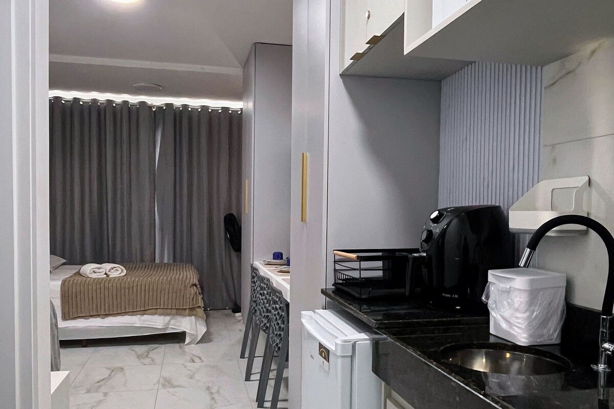 A compact hotel room with a bed, a small kitchenette, a bathroom, and a view of the street.