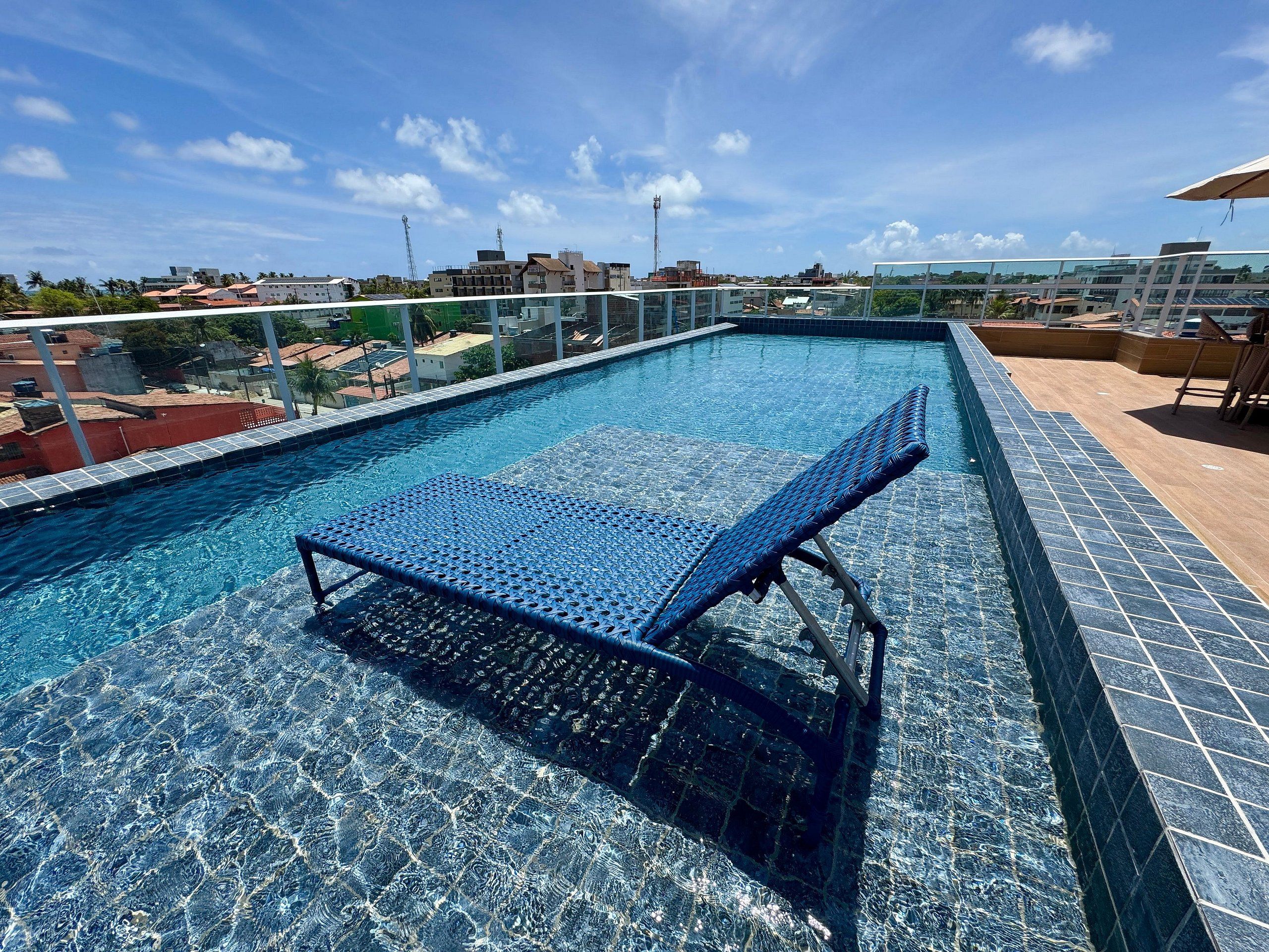 Ein Dachpool mit Glasabschottung, einer Liege und Blick auf die Stadtlandschaft.