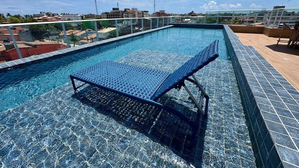 A rooftop swimming pool with a glass barrier, a lounge chair, and a view of the cityscape. - Waikiki Garden (Ipojuca)