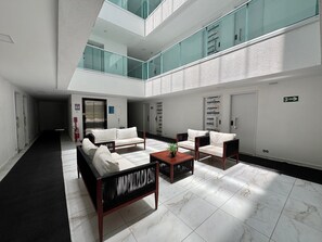 A modern lobby with a central seating area, glass railings, and a visible elevator. - Waikiki Garden (Ipojuca)