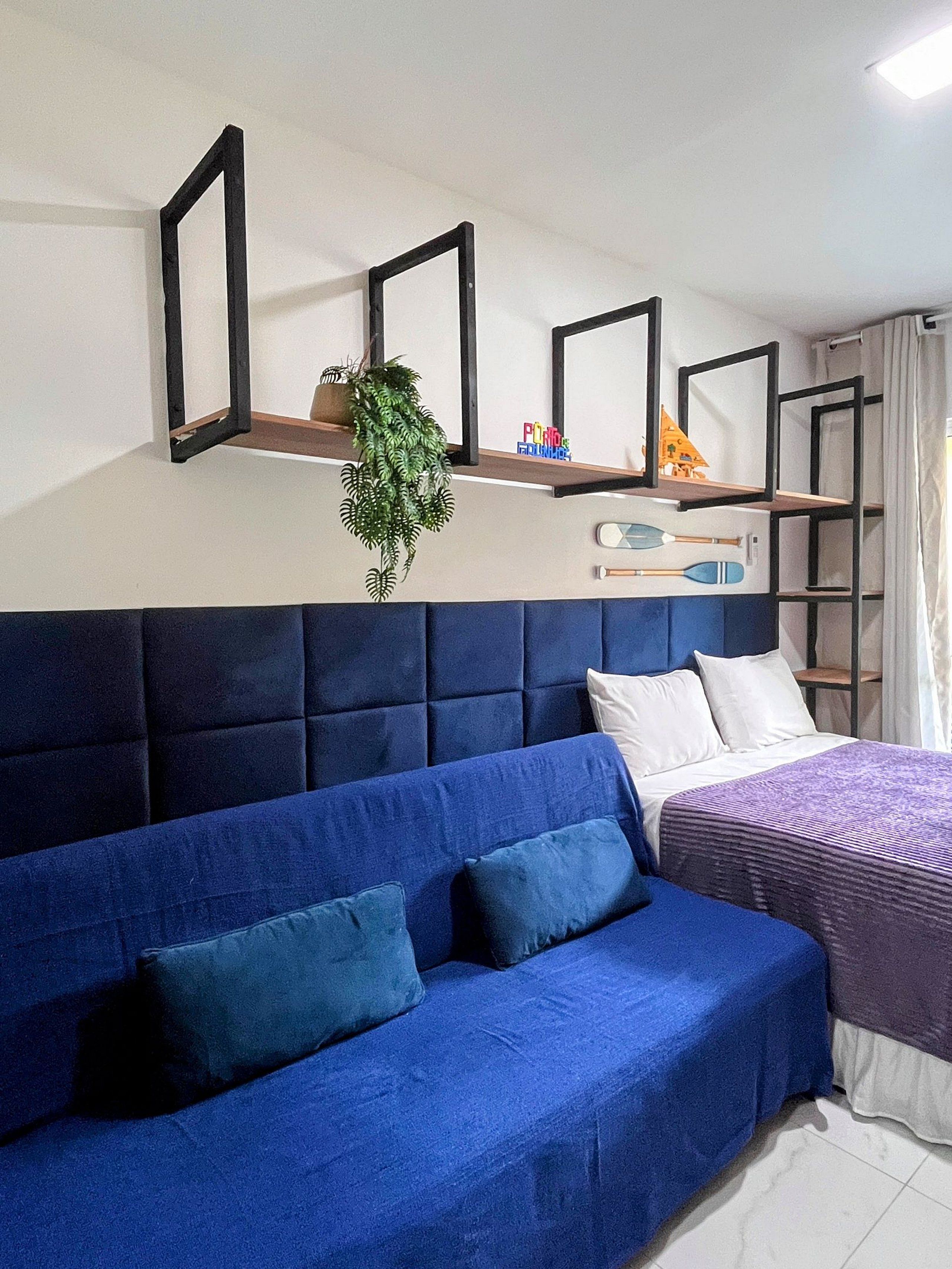 Una habitación con un sofá azul, una cama con cubrecama púrpura y una estantería con una planta y juguetes infantiles.