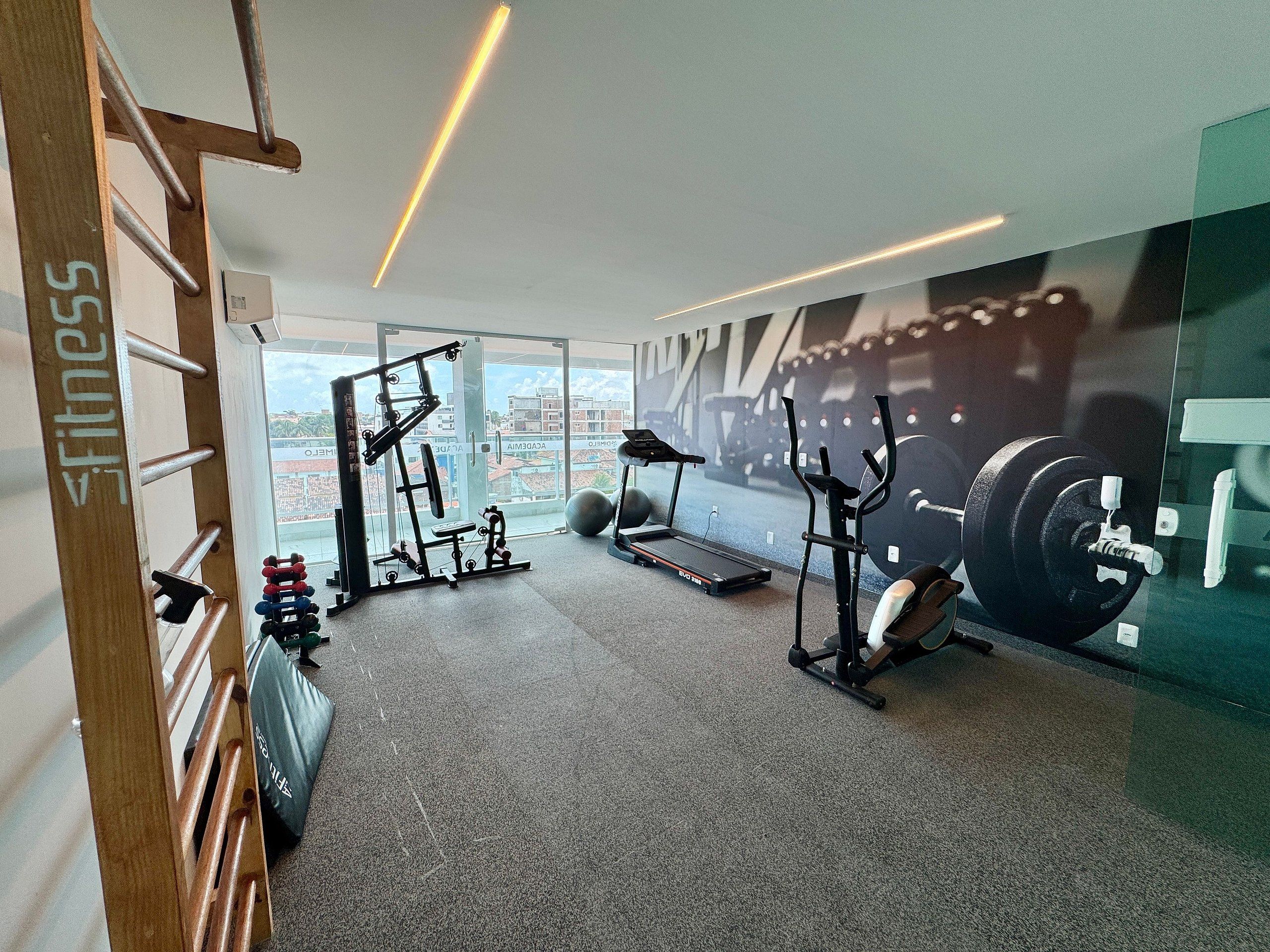 A gym with exercise equipment, a treadmill, and a large window with a city view.