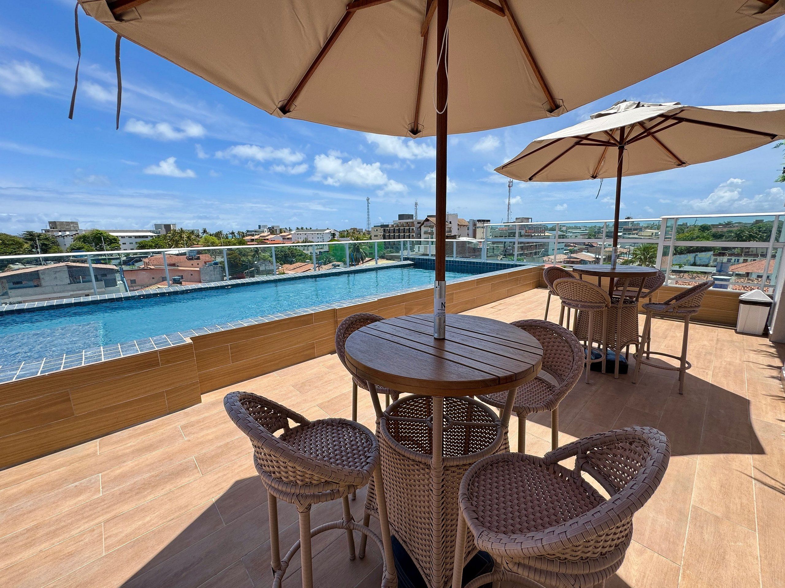 A rooftop terrace with a pool, wicker furniture, and a view of the city.