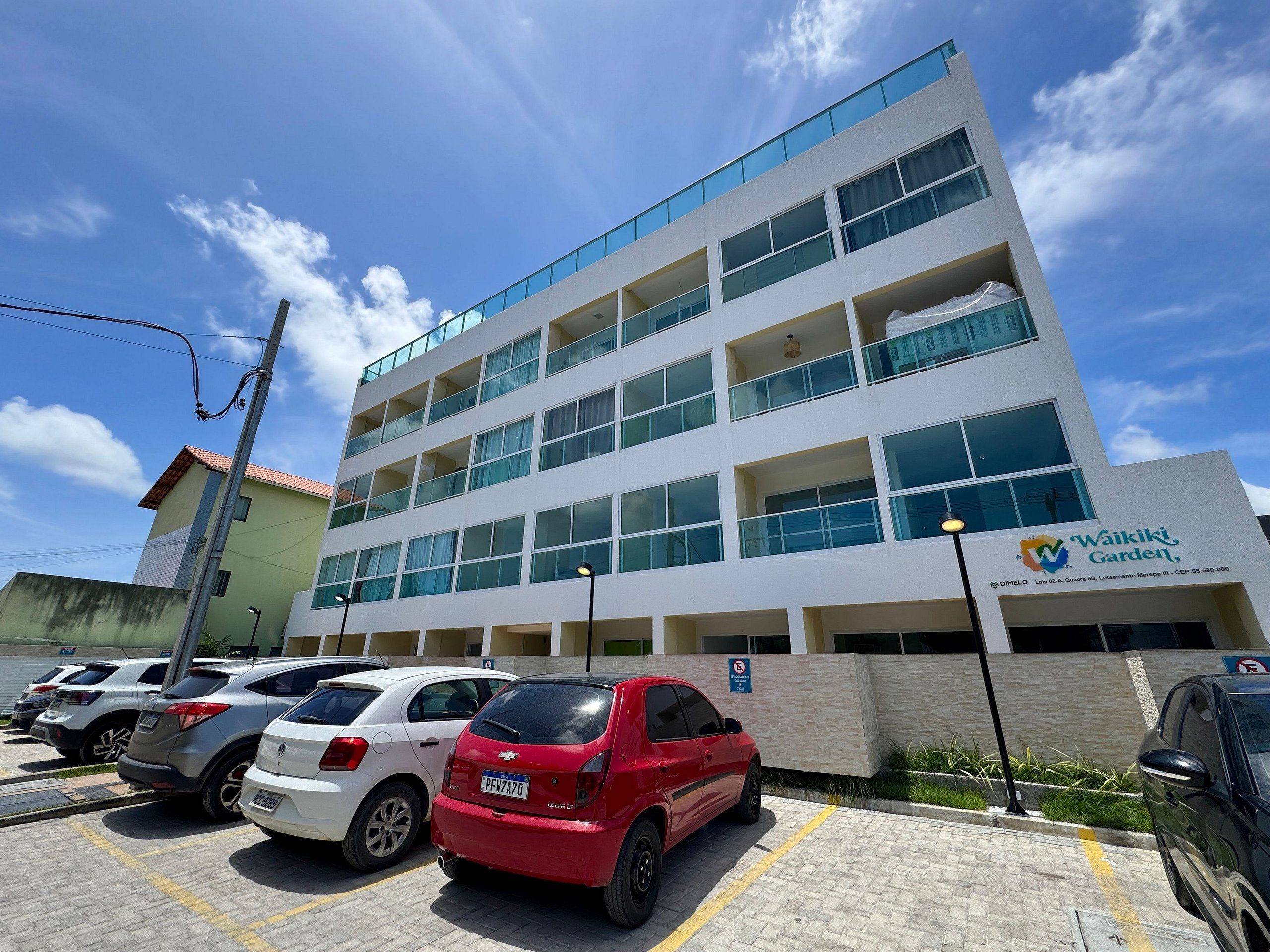 A multi-story building with a sign for Waikiki Garden, a parking lot with several cars, and a clear blue sky.