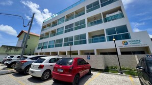 A multi-story building with a sign for Waikiki Garden, a parking lot with several cars, and a clear blue sky. - Waikiki Garden (Ipojuca)