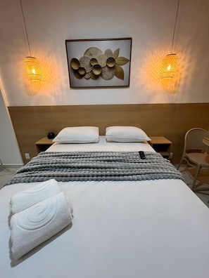 A hotel room with a bed, two bedside tables, a wall-mounted artwork, and two wall-mounted lamps. - Waikiki Garden (Ipojuca)